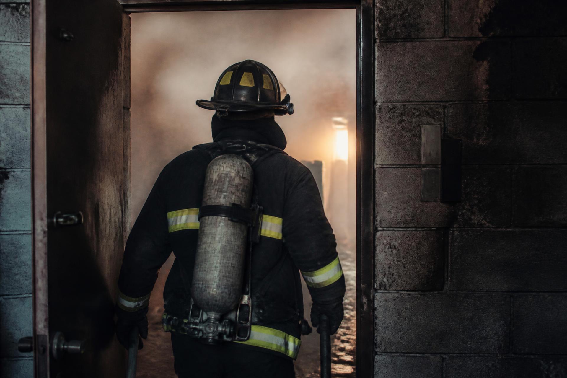 Firefighter in turnout gear walking into a smoke-filled doorway